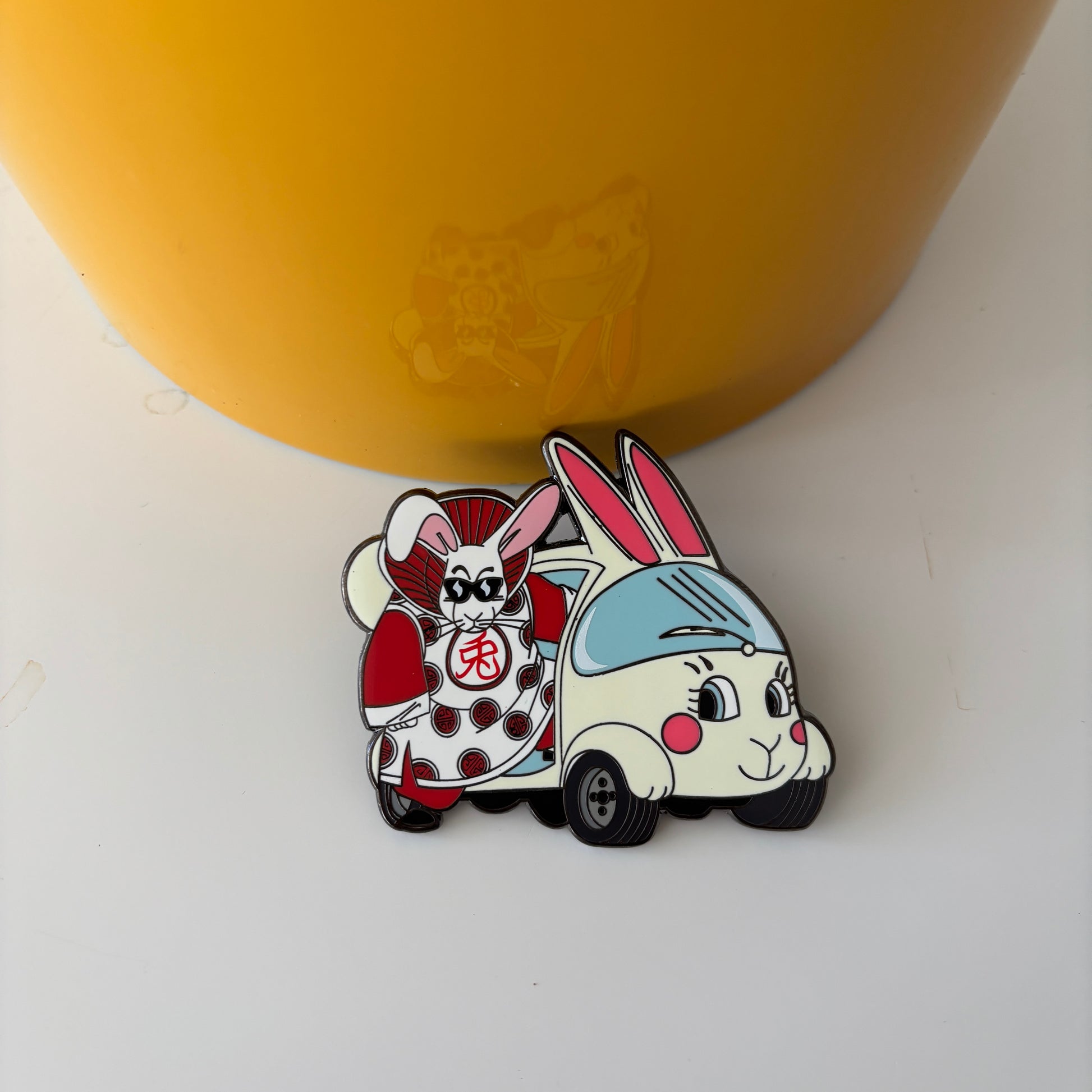 cartoon pins of a rabbit and a car on a white surface with a yellow container in the background.