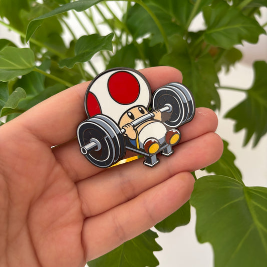 Pin with cartoon mushroom lifting weights held in a hand against a leafy green background