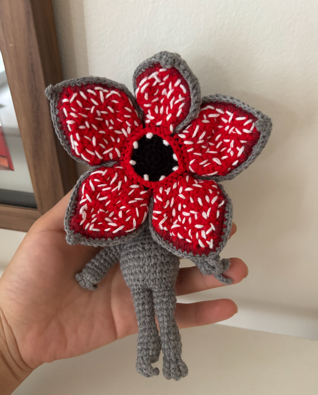 Hand holding a red and gray crochet flower against a neutral background