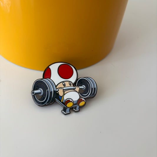 Enamel pin with character mushroom lifting weights on a white background