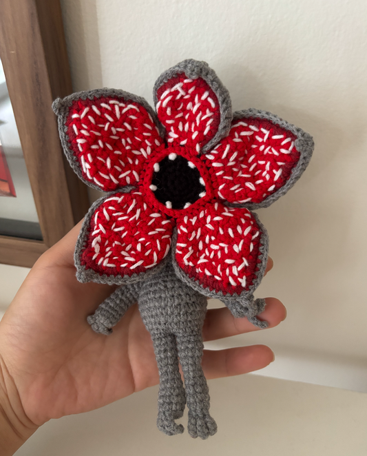 Hand holding a red and gray crochet flower against a neutral background